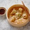 Delicious chinese dumplings served in wooden bamboo steamer with chopstick and soy sauce. Placed on stone background.